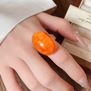 Close-up view of a vintage orange resin oval ring worn on a finger for elegant detail