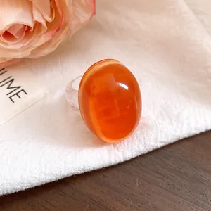 Close-up detail of a vintage oval resin ring in vibrant orange with a clear band.