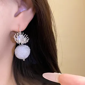Macro view showing the intricate crystal flower and textured round white earring pendant.