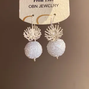 Detailed macro view of crystal flower earrings with white textured spherical pendants
