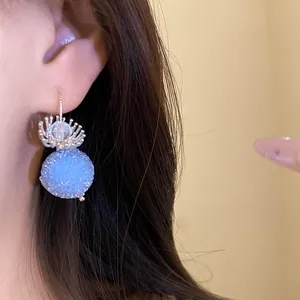 Close-up detail of a light blue beaded spherical earring featuring a silver floral top