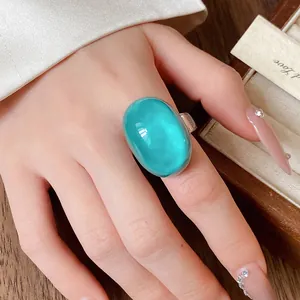 Detailed close-up showing a large teal oval resin ring worn on a finger with a luxury aesthetic.