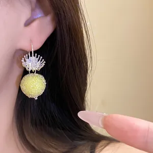 Close-up of yellow round textured earring with crystal flower detail worn on ear
