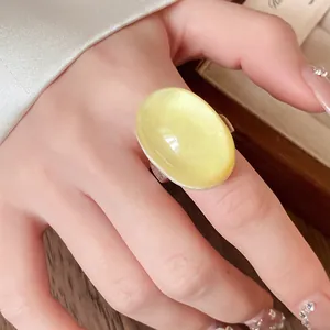 Macro view of a large vintage oval pale yellow resin ring on a woman's finger with silk background