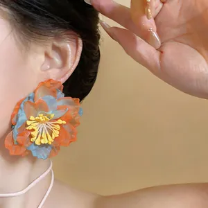 Close-up detail of a vibrant orange and blue chiffon flower stud earring on a model.