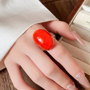 Close-up of a glossy orange oval resin ring worn on a hand with elegant nail art.