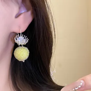 Close-up detail of textured yellow round ball earrings with crystal accents on a model