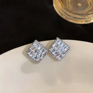 Macro detail of French style diamond-shaped zircon stud earrings on a beige surface.