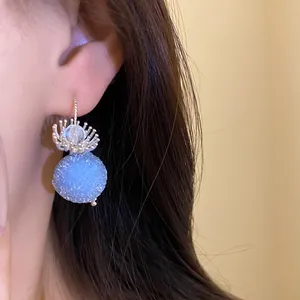 Detailed close-up showing a light blue textured round drop earring with floral cap on an ear