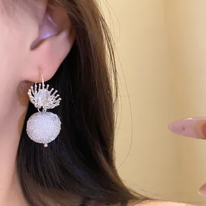 Close-up of elegant crystal flower earrings with white round bead pendants on model