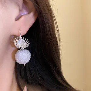 Close-up detail showing crystal flower pendant earrings with textured white sphere drop