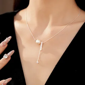 Detail view of the silver necklace featuring a textured bar and pearl pendant on a model.