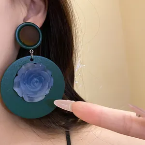 Primo piano di orecchini pendenti vintage in resina con rosa blu su cerchio verde.
