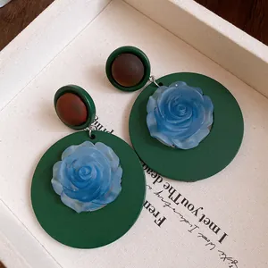 Primo piano di orecchini vintage in resina verde scuro con dettagli di rose blu in resina.