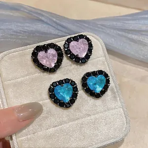 Detailansicht von rosa und blauen Herzohrsteckern mit schwarzem Rand in einer beigen Box.