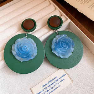 Dettaglio macro di orecchini vintage con rosa in resina blu su base tonda verde scuro