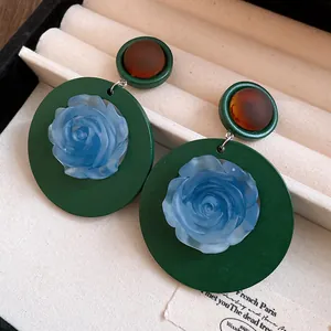 Primo piano di orecchini retrò in resina con rosa blu su base verde scuro elegante.