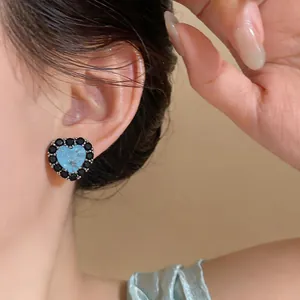 Detailaufnahme von hellblauen Herzohrringen mit schwarzen Zirkonia-Steinen am Ohr.