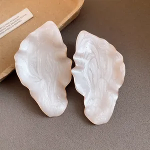 Detail of irregular leaf-shaped stud earrings with a pearlescent white enamel finish.