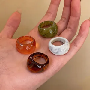 Gros plan de quatre bagues en résine colorées aux textures marbre et ambre