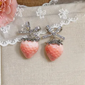 Close-up of sweet resin strawberry earrings with sparkling zircon bow detail