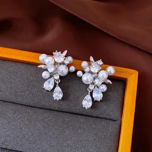 Elegant silver-toned earrings with zircons and pearls on a display tray