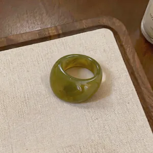 Gros plan d'une bague épaisse en résine vert olive avec texture marbre sur support beige