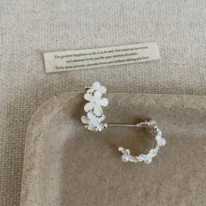 Primo piano di eleganti orecchini a cerchio a C con fiori e perle su sfondo naturale