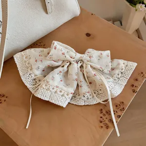 Detail van bloemenstoffen haarklem met witte kanten rand en lange linten.