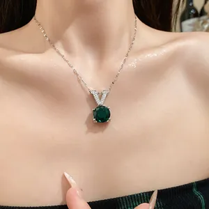 Détail d'un collier en argent avec lettre V et un pendentif rond en pierre verte