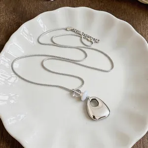 Close-up view of a silver geometric smooth pendant necklace with clear and white beads