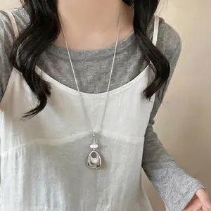 Close-up detail of a minimalist silver geometric teardrop pendant sweater chain on a model