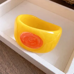 Close-up of an elegant yellow resin bangle bracelet with orange swirl enamel detail.