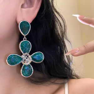 Detailed close-up of a large green resin flower drop earring worn by a female model