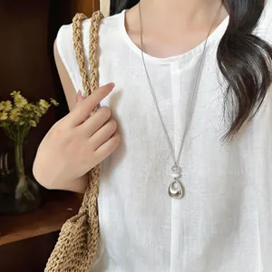 Detailed view of a silver geometric pendant necklace worn over a white linen shirt.