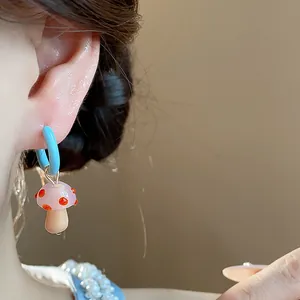 Close-up detail of a blue hoop earring with a cute pink glass mushroom charm worn on ear
