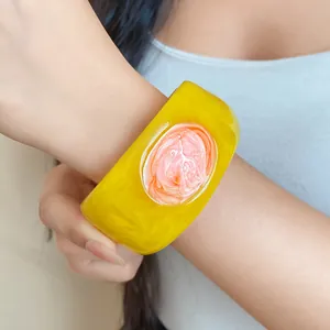 Detailed view of a yellow resin bangle with a marble pink circular design on the wrist.