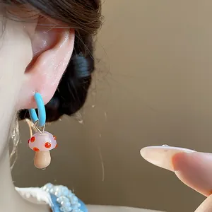 Close-up detail of a light blue enamel hoop earring with a pink glass mushroom charm.
