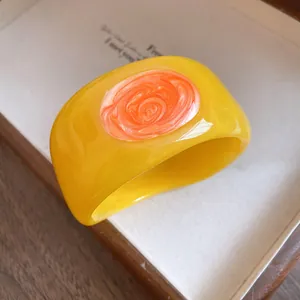 Close-up detail of yellow resin bangle featuring a vibrant orange swirl design element