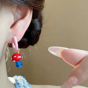 Detail view of a red and blue mushroom hoop earring in colorful enamel glass material.