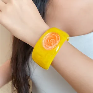 Elegant detail view of a vibrant yellow resin bangle with an orange swirl design on wrist