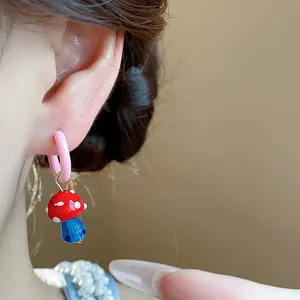Close-up of a cute red and blue enamel mushroom earring charm on a pink hoop.