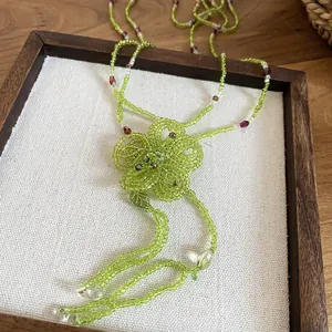 Close-up of a handmade green glass beaded necklace featuring a flower and tassel design