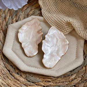 Elegant leaf-shaped resin stud earrings with gold-plated edges shown on a woven tray