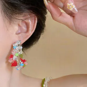 Detail view of colorful ethnic-style beaded flower hoop earrings on a model's ear.