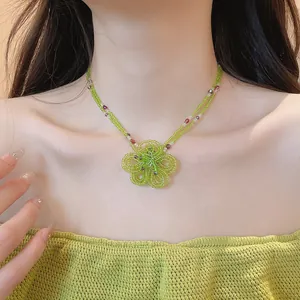 Detail view of a green beaded flower necklace on a model's neck for a vacation look