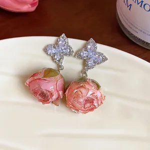 Close-up of zircon butterfly earrings with delicate pink immortal rose flower drops