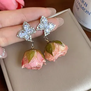 Close-up detail of silver butterfly zircon earrings with pink preserved rosebud drops.