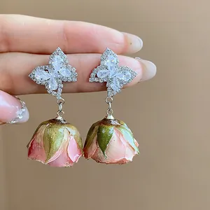 Exquisite close-up of zircon butterfly studs with dangling preserved pink rose bud earrings.