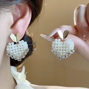 Detail view of elegant heart-shaped pearl earrings with gold studs and crystal accents.